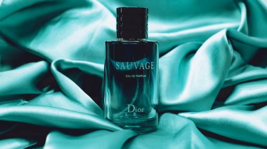 Bir şişe Dior Sauvage Eau de Parfum pürüzsüz, gök mavisi renkli saten bir kumaşa konur..