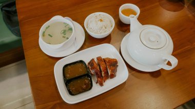 Bir çaydanlık, bir fincan çay, bir kase pirinç, kızarmış et dilimleri ve ahşap bir masada iki sosun yer aldığı geleneksel bir Asya yemeği dengeli ve iştah açıcı bir yemek deneyimi sunuyor..