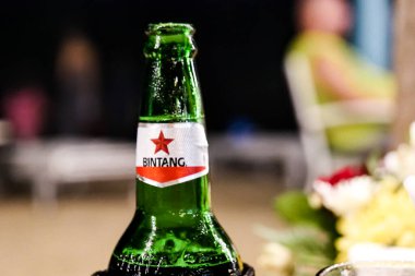 Görüntü yeşil bir Bintang bira şişesinin yakın çekimini gösteriyor. Kırmızı yıldız logosu ve bulanık bir arka plan..
