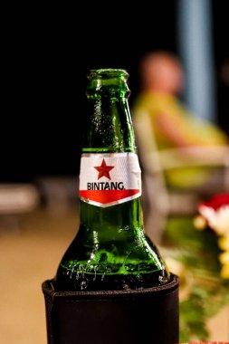 Görüntü yeşil bir Bintang bira şişesinin yakın çekimini gösteriyor. Kırmızı yıldız logosu ve bulanık bir arka plan..