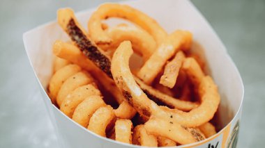 Beyaz kağıt bir kabın içinde servis edilen baharatlı, kıtır kıtır, altın sarısı kıvırcık patates kızartması..