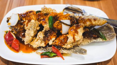 Beyaz tabakta servis edilen, domates, ananas ve kırmızı biber dilimleriyle süslenmiş gevrek, tatlı ve ekşi gurami balığı. Zarif bir sunumda leziz bir lezzet karışımı.