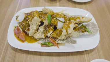 Beyaz tabakta servis edilen, domates, ananas ve kırmızı biber dilimleriyle süslenmiş gevrek, tatlı ve ekşi gurami balığı. Zarif bir sunumda leziz bir lezzet karışımı.