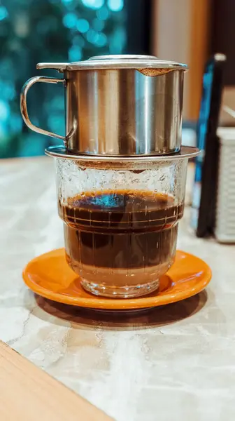 Sütlü kahve dolu bir bardak. Üstte bir kahve filtresi var ve damlalar aşağıdaki bardağa dökülüyor..