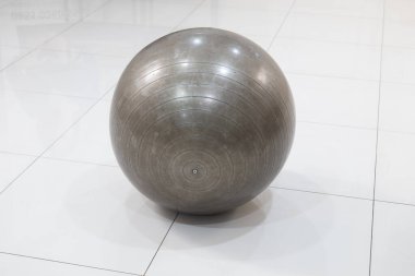 Eşmerkezli daireleri olan büyük gri bir egzersiz topu el değmemiş, beyaz fayanslı bir zeminde oturur ve modern kapalı bir ortamda ışığı yansıtır..