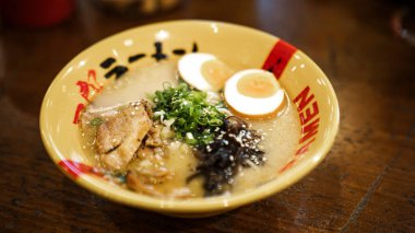 Kıtır soğan halkalarının yakın planda, kremalı sarı bir kâse içinde ramen ile servis edilmesi, yemeğin dokusunu ve iştah açıcı sunumunu vurguluyor..
