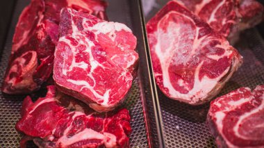 Bir kasaptaki delinmiş metal tepsilerde sergilenen mermerli çiğ bifteklerin yakın çekimi etin kalitesini ve tazeliğini gözler önüne seriyor..