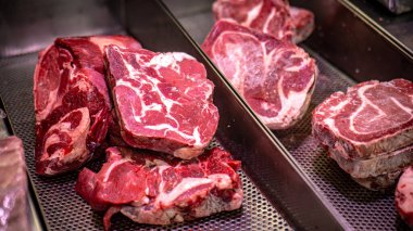 Bir kasaptaki delinmiş metal tepsilerde sergilenen mermerli çiğ bifteklerin yakın çekimi etin kalitesini ve tazeliğini gözler önüne seriyor..