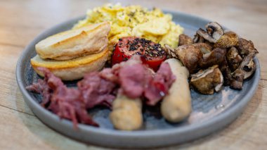 Yağda yumurta, sosis, mantar, tost ekmeği, ızgara domates ve domuz pastırması içeren doyurucu bir İngiliz kahvaltısı. Tatmin edici ve geleneksel bir sabah yemeği için mükemmel..
