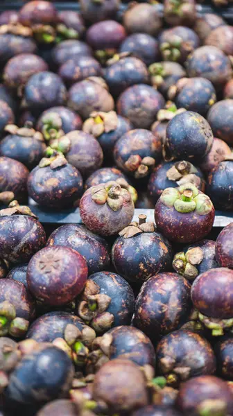 Markette sergilenen canlı mor derili ve yeşil saplı taze mangosteen meyvelerinin yakın plan görüntüsü. Meyveler yoğun bir şekilde paketlenmiş, eşsiz dokularını ve renklerini sergiliyorlar..