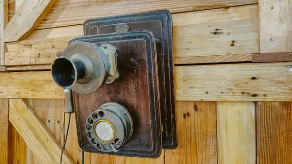 Çevirmeli bir kadranı, ahşap bir arka plakası ve ahşap bir duvarda siyah bir ağızlık olan antika duvara monte edilmiş bir telefon. Eski tasarım, tarihsel işçiliği ve erken iletişimi vurguluyor..