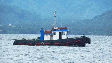 Donggala Körfezi, Merkez Sulawesi 'de bir römorkör. Sakin bir su kütlesinin üzerinde süzülür. Dağlık, ormansı bir arka planı vardır..