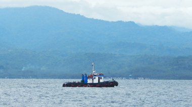 Donggala Körfezi, Merkez Sulawesi 'de bir römorkör. Sakin bir su kütlesinin üzerinde süzülür. Dağlık, ormansı bir arka planı vardır..