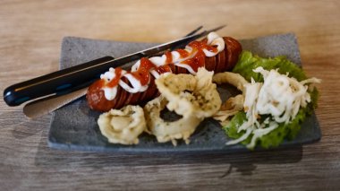 Bir tabak sulu sosis yanında kızarmış soğan ve kremalı mayonez serpiştirilmiş ferahlatıcı bir salata. Tatmin edici bir yemek için leziz bir lezzet ve doku karışımı..