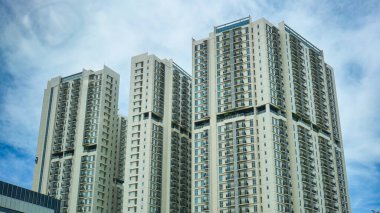 Parlak mavi bulutlu gökyüzünün arka planında yükselen apartman binaları.