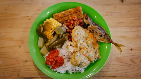 Bu öğle yemeğinin menüsünde pirinç var. Kızarmış balık, tofu, tempeh ve sebze var. Mısır ve sambal da dahil..