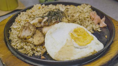 Nasi Goreng 'in ağız sulandırıcı bir tabağı, yanında salatalık dilimleri, domates ve krakerler ile birlikte, yanında küçük bir kase soya sosu ile birlikte, siyah bir tabakta servis edilir..