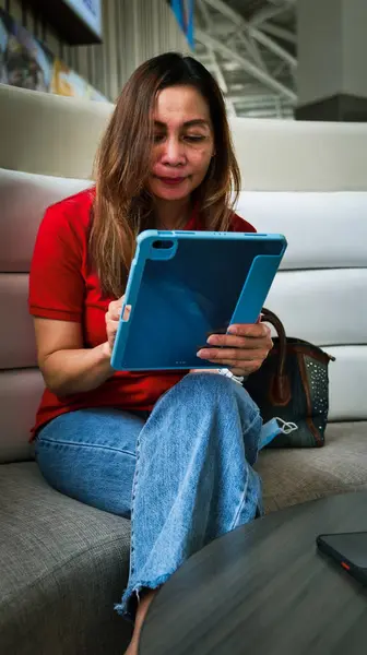 Kırmızı elbiseli bir kadın, yemek katında, çalışırken ve tablet tutarken..