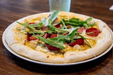 Carciofi e pepperoni pizza, kremalı soslu enginar, pepperoni, salam ve mozzarella peyniri. Üstü roket yapraklarıyla kaplı.