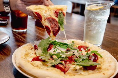 İçinde krema sosu, pepperoni eti, salam eti, mozzarella peyniri ve kekik otu bulunan Carciofi e pepperoni pizzası. Üstü roket yapraklarıyla kaplı.