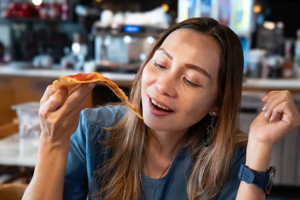Mavi elbiseli ve omuz hizasında saçlı güzel bir kadın elinde bir dilim pizza yiyordu..