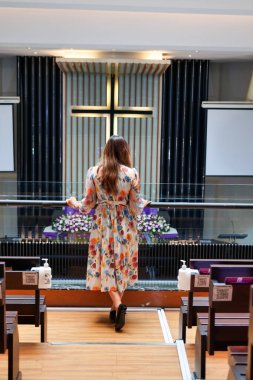 Omuz hizasında sarı saçlı güzel bir kadın kilisedeydi. Duvarda bir haç var..