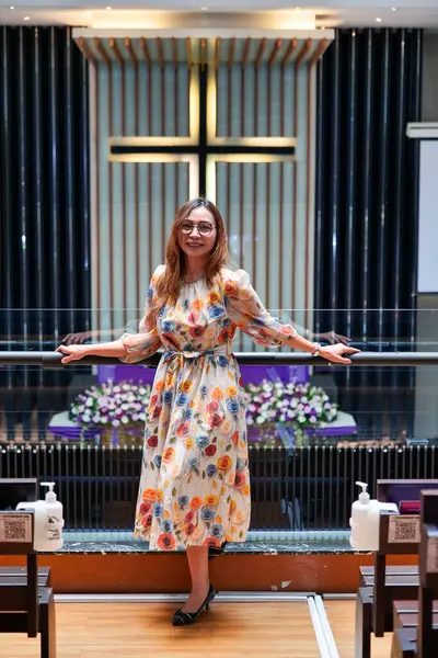 Omuz hizasında sarı saçlı güzel bir kadın kilisedeydi. Duvarda bir haç var..