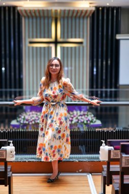 Omuz hizasında sarı saçlı güzel bir kadın kilisedeydi. Duvarda bir haç var..