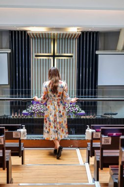 Omuz hizasında sarı saçlı güzel bir kadın kilisedeydi. Duvarda bir haç var..