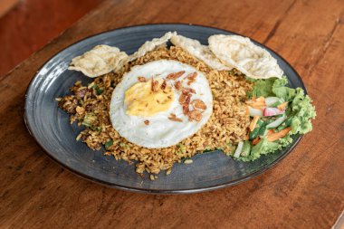 Ahşap bir masada seramik tabakta servis edilen bir restoranda kızarmış pirinç. Kızarmış pirinç yumurta, dilimlenmiş tavuk, sebze, turşu ve patates kızartması içerir..