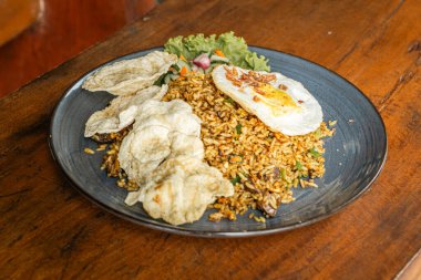 Ahşap bir masada seramik tabakta servis edilen bir restoranda kızarmış pirinç. Kızarmış pirinç yumurta, dilimlenmiş tavuk, sebze, turşu ve patates kızartması içerir..