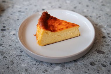 Mermer bir masada beyaz bir seramik tabakta servis edilen bir dilim cheesecake..