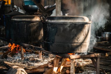 Büyük, yanmış görünümlü bir kazan yakacak odunla yemek pişirmek için kullanılıyor. Duman sobayı doldurur, güneş ışığıyla aydınlatır..