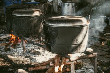 Büyük, yanmış görünümlü bir kazan yakacak odunla yemek pişirmek için kullanılıyor. Duman sobayı doldurur, güneş ışığıyla aydınlatır..