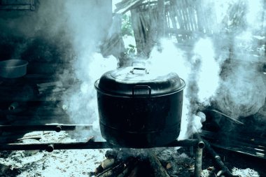 Büyük, yanmış görünümlü bir kazan yakacak odunla yemek pişirmek için kullanılıyor. Duman sobayı doldurur, güneş ışığıyla aydınlatır..