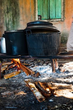 Büyük, yanmış görünümlü bir kazan yakacak odunla yemek pişirmek için kullanılıyor. Duman sobayı doldurur, güneş ışığıyla aydınlatır..