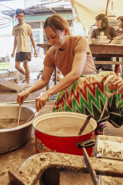 Batik sarong giyen bir kadın sago bazlı yiyecek işliyor, Kapurung. Bu yemeğin çiğnenmiş bir dokusu var..