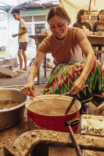 Batik sarong giyen bir kadın sago bazlı yiyecek işliyor, Kapurung. Bu yemeğin çiğnenmiş bir dokusu var..