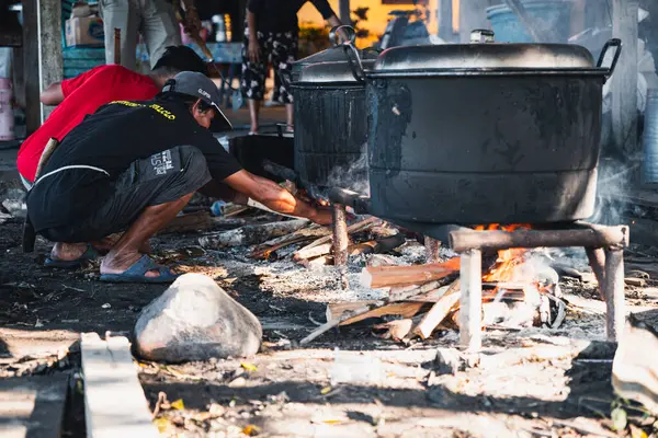 Bir adam büyük bir kazanda yemek pişirmek için odun yakıyor..