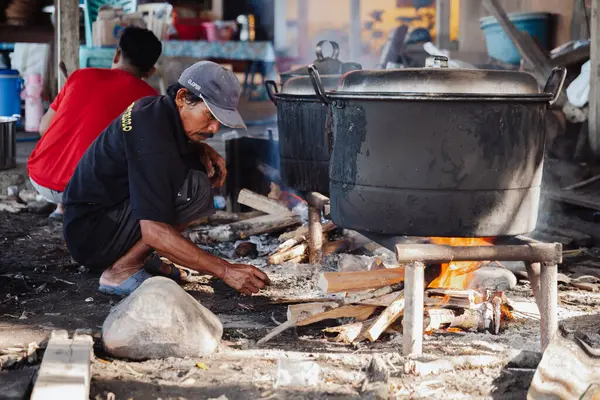 Bir adam büyük bir kazanda yemek pişirmek için odun yakıyor..