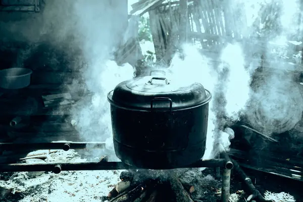 Büyük, yanmış görünümlü bir kazan yakacak odunla yemek pişirmek için kullanılıyor. Duman sobayı doldurur, güneş ışığıyla aydınlatır..