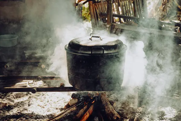 Büyük, yanmış görünümlü bir kazan yakacak odunla yemek pişirmek için kullanılıyor. Duman sobayı doldurur, güneş ışığıyla aydınlatır..