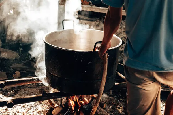 Bir adam hortumla büyük bir kazana su koyuyor. Bu kazan, yakacak odun ısıtmalı kaynar su için..