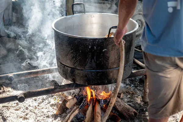 Bir adam hortumla büyük bir kazana su koyuyor. Bu kazan, yakacak odun ısıtmalı kaynar su için..