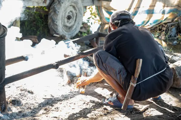 Beline palayla bağlanmış yaşlı bir adam yakacak odun yakıyor. Kazan kullanarak yemek pişirmek için kullanılacak..