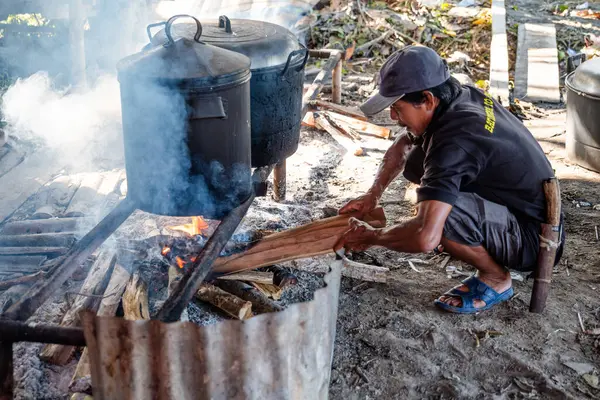 Beline palayla bağlanmış yaşlı bir adam yakacak odun yakıyor. Kazan kullanarak yemek pişirmek için kullanılacak..