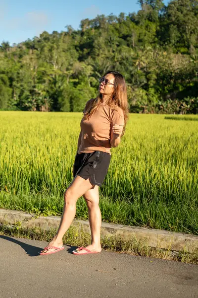 Güzel bir kadın arkasında pirinç tarlalarıyla güneşin tadını çıkarıyor..