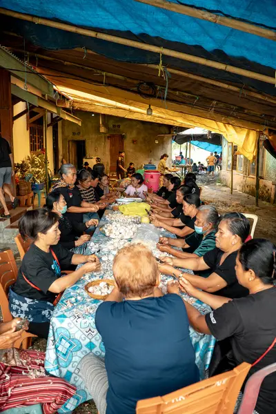 Bir grup kadın uzun bir masada oturuyor ve baharat olarak kullanılacak sarımsakları soyuyorlar..