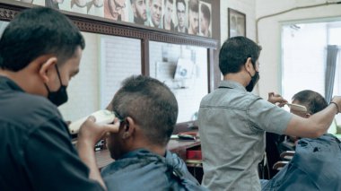 Men's barber shop activities during the day. A man wearing a blue cloth is being shaved by a barber.