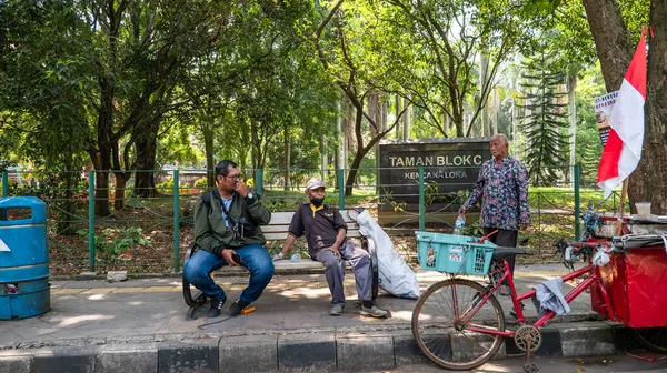 Bazı adamlar parkın yanında sohbet ediyorlardı. Önlerinde kırmızı ve beyaz bayrak taşıyan bisiklet itişli bir araba var..